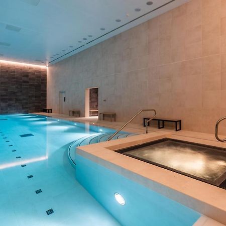 Citysuites 2 Aparthotel Mánchester Exterior foto The photo shows an indoor swimming pool area. The pool is a bright blue color and features smooth, tiled surfaces. On one side, there is a hot tub area with steps leading into it. The walls are made of light-colored stone, and there is ambient lighti