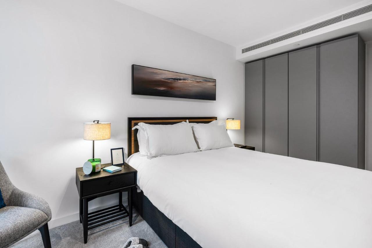 Citysuites 2 Aparthotel Mánchester Exterior foto The photo shows a modern bedroom with a neatly made bed featuring white linens and pillows. Flanking the bed are two bedside tables, each with a lamp providing soft lighting. There is a piece of artwork above the bed, which appears to depict a landsc