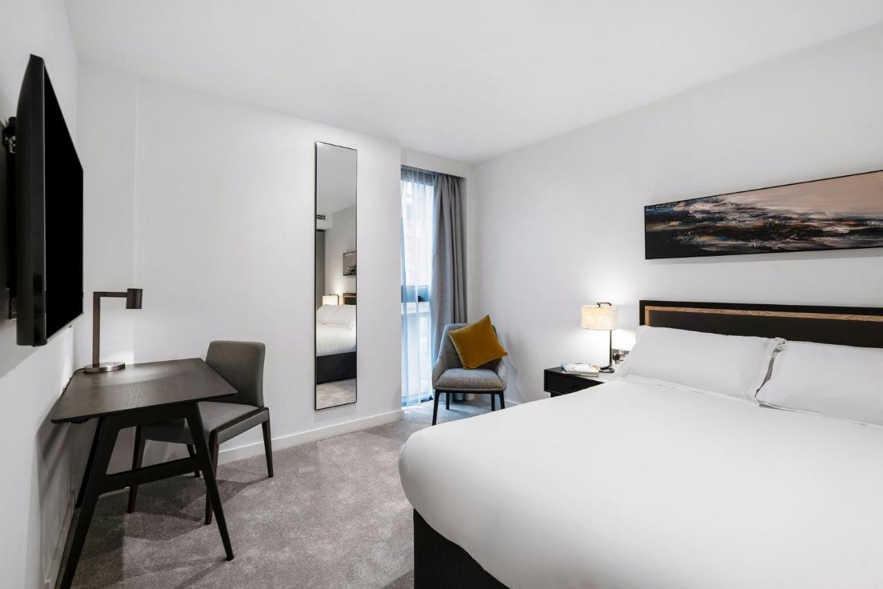Citysuites 2 Aparthotel Mánchester Exterior foto The photo shows a modern hotel room with a clean and minimalist design. It features a large bed with white linens, a small desk with a chair, and a mirror mounted on the wall. There is a chair in one corner with a decorative pillow, and the room has 