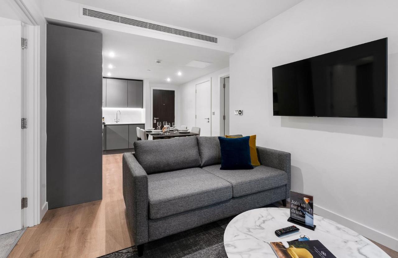 Citysuites 2 Aparthotel Mánchester Exterior foto The photo shows a modern living space that includes a gray sofa with colorful cushions, a round marble coffee table, and a flat-screen TV mounted on the wall. In the background, there is a kitchen area featuring sleek cabinets. The flooring is light 