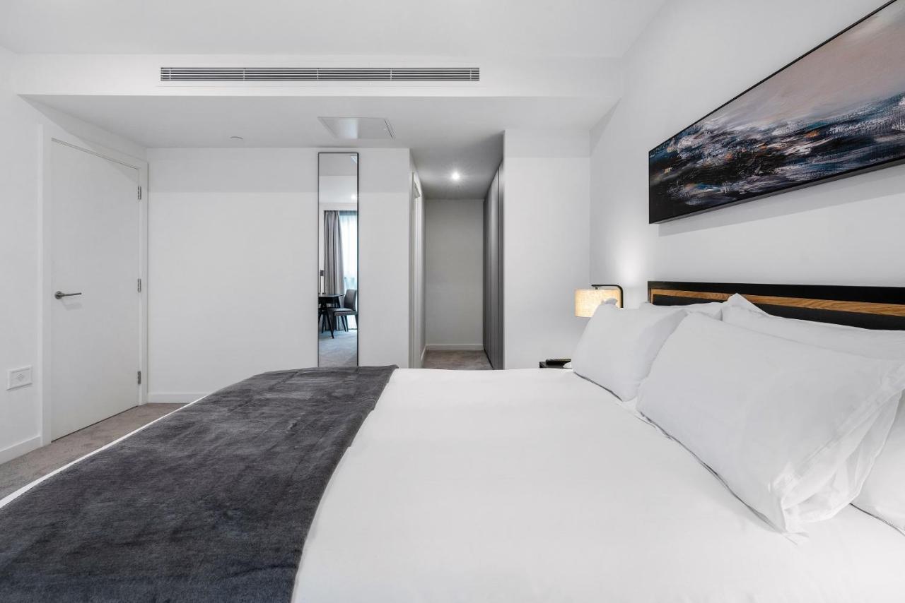 Citysuites 2 Aparthotel Mánchester Exterior foto The photo shows a modern bedroom with a minimalistic design. In the foreground, there is a neatly made bed with white linens and a dark gray throw blanket. To the side, there is a bedside lamp and a piece of abstract artwork on the wall above the bed
